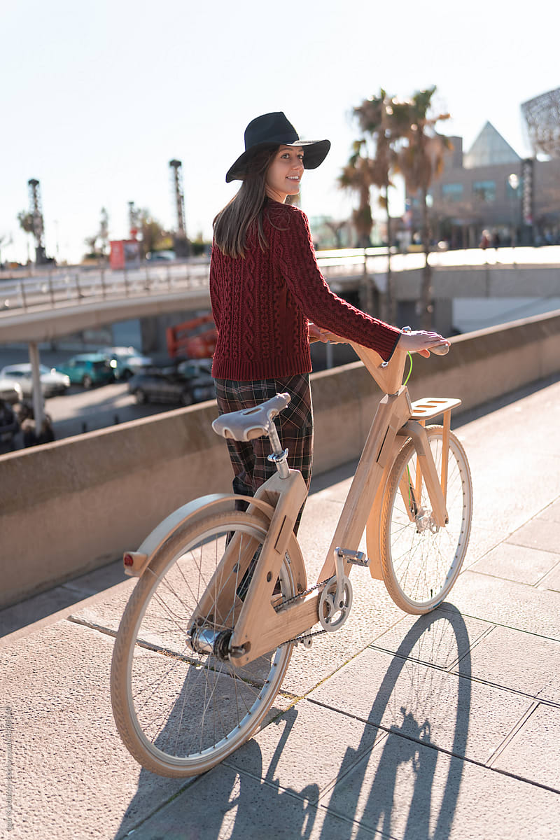 Cheerful woman with wooden bicycle walking on bridge