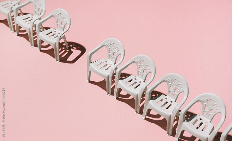 One chair missing in line of chairs on pink background.