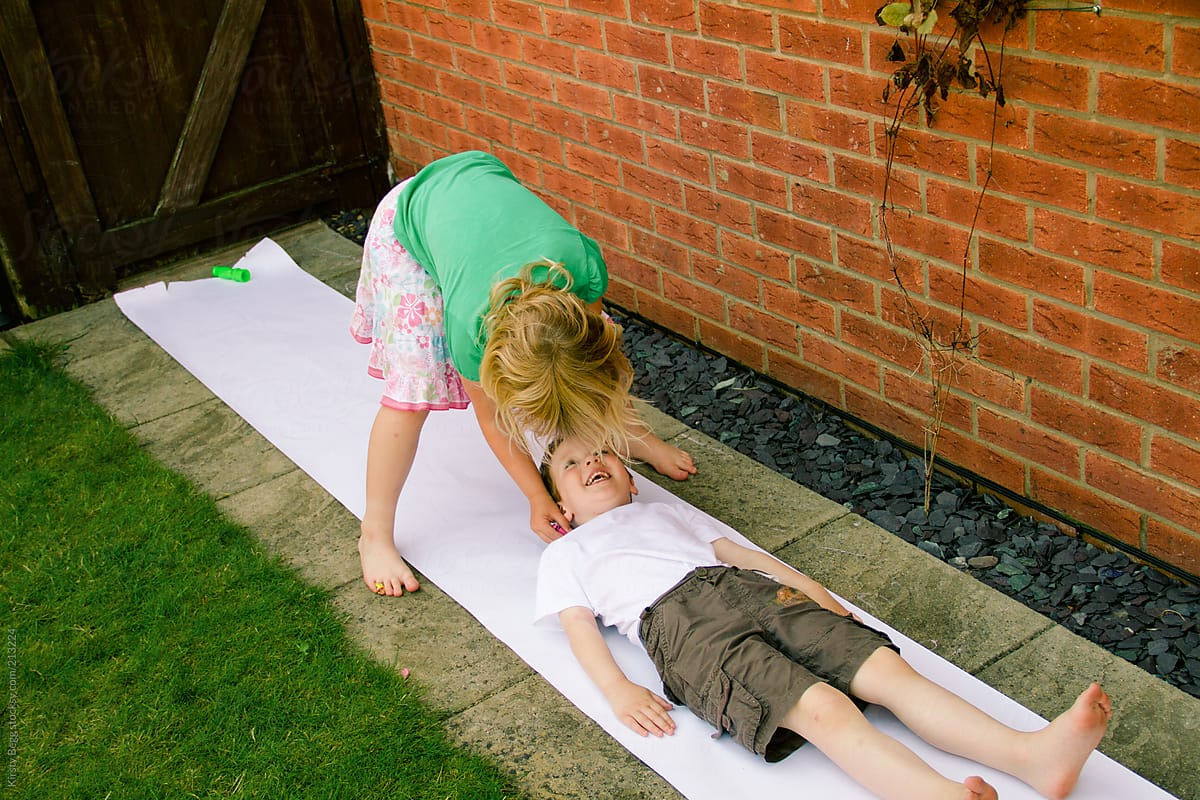 A girl draws the outline of her brother on paper in the garden