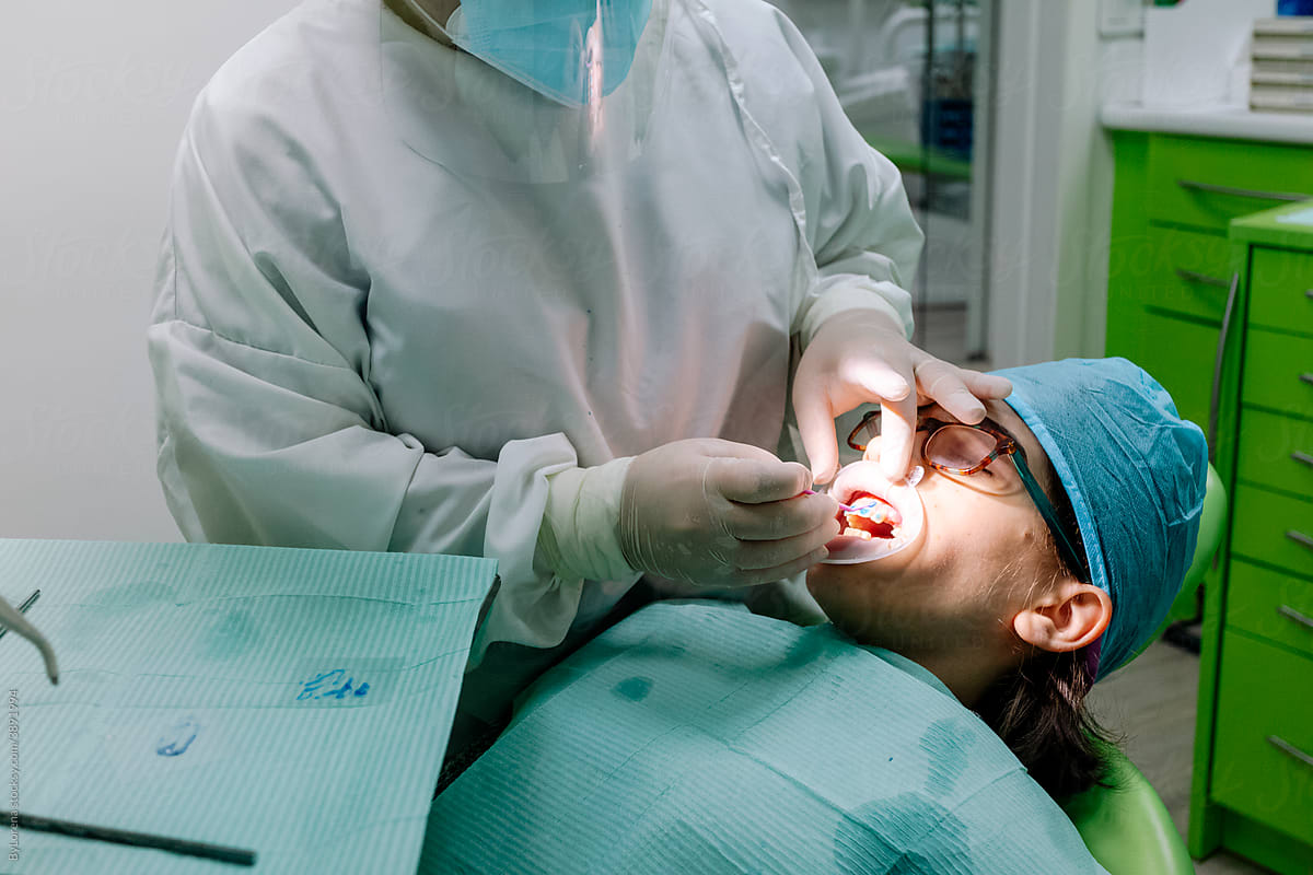 Crop orthodontist applying glue on teeth of patient