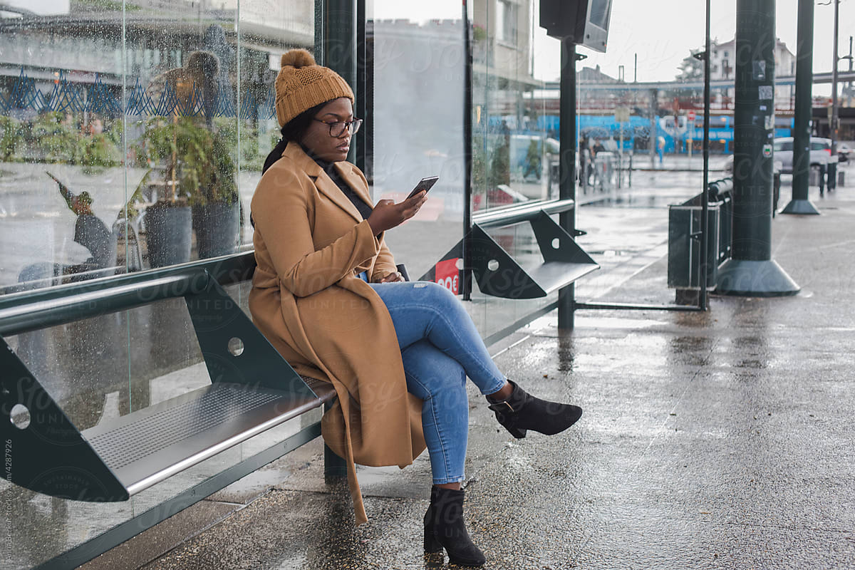 woman using smartphone on bus stop in winter, transport