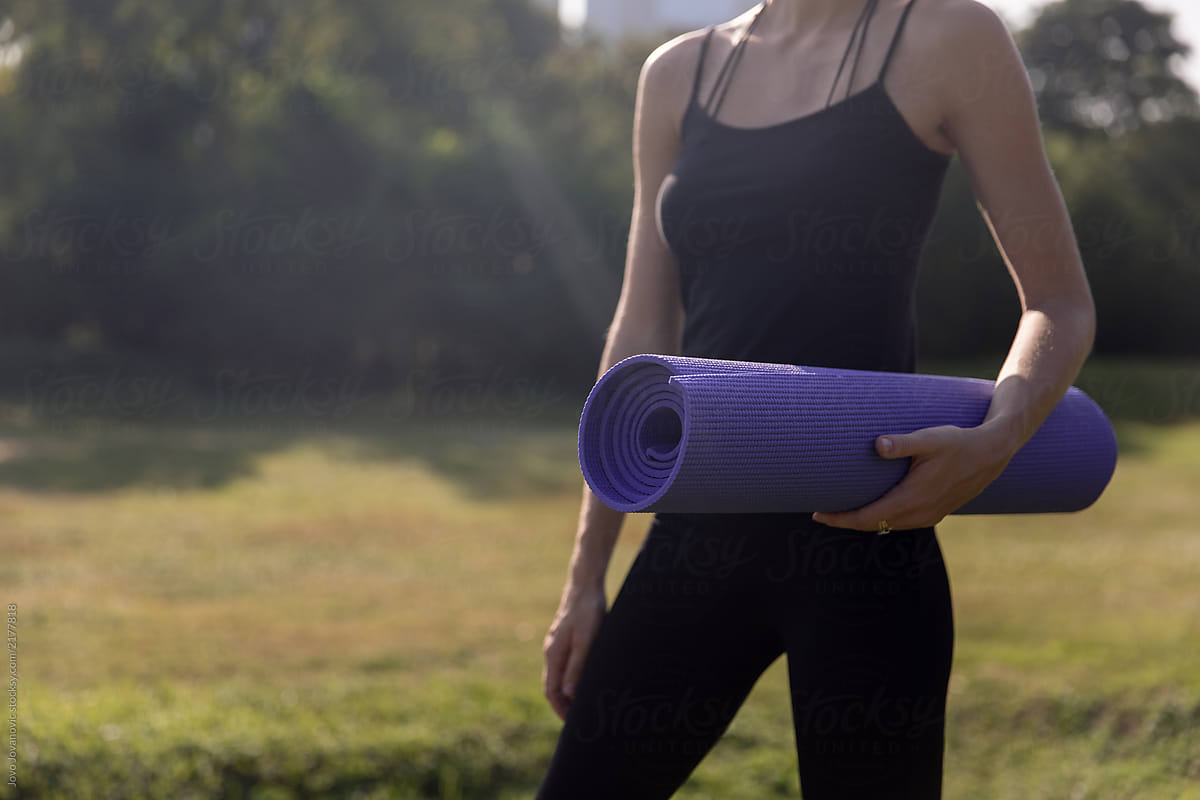 Woman holding yoga mat alone in the park