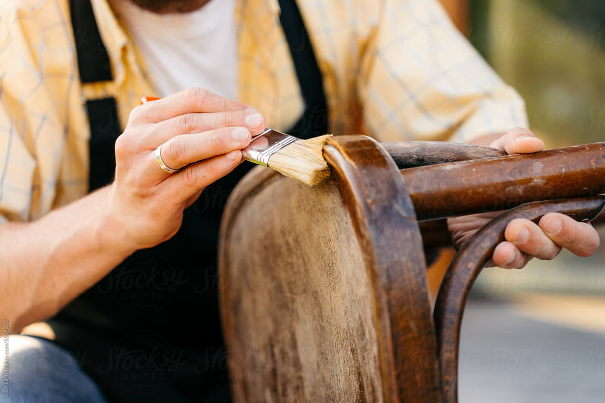 A man varnishes a chair outdoors