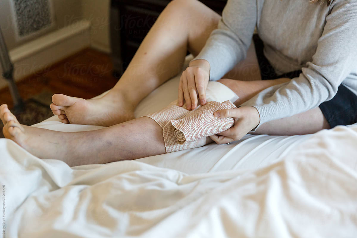 Woman unwraps bandaged knee.
