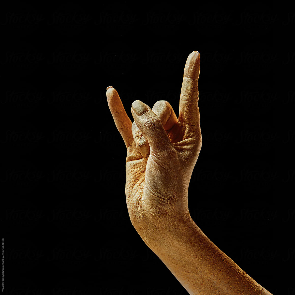 Raised hand of a girl in gold dust shows a rock sign on a black background with copy space.