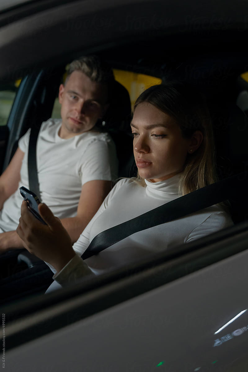 Pregnant Woman With Husband Looking At The Phone Sitting in the Car