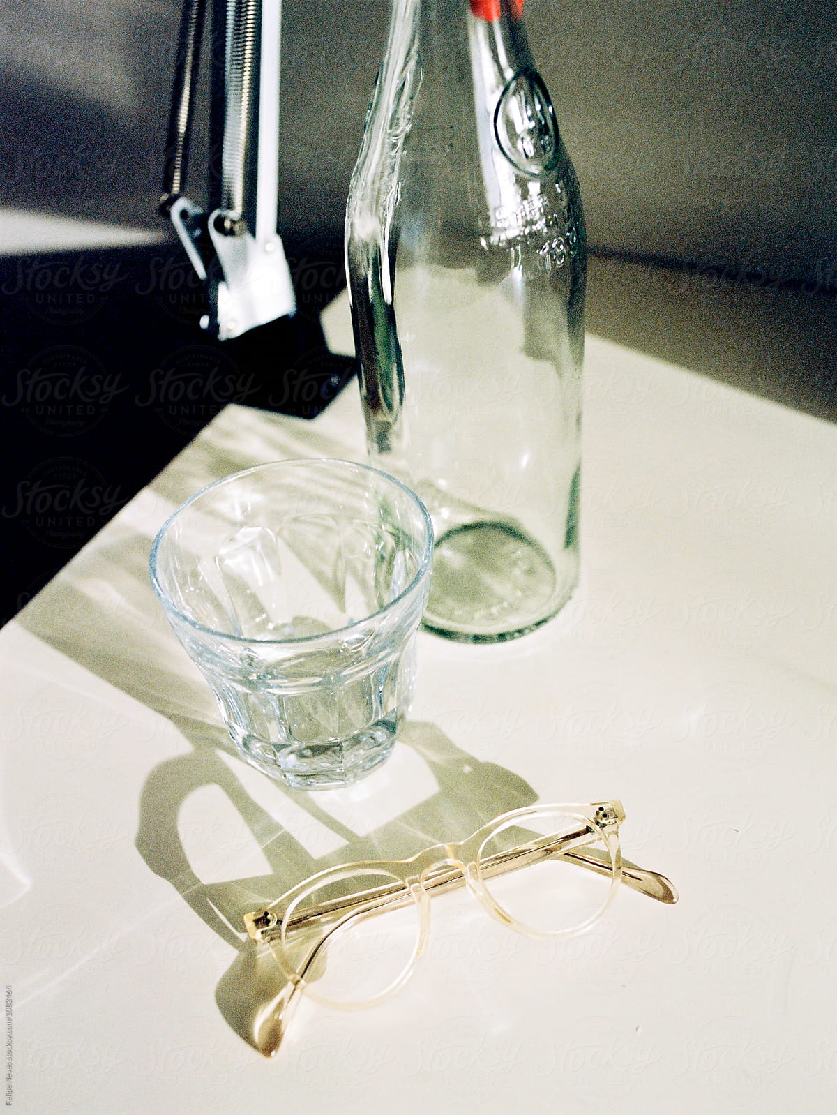 Glass water bottle, water glass and pair of prescription glasses on a table