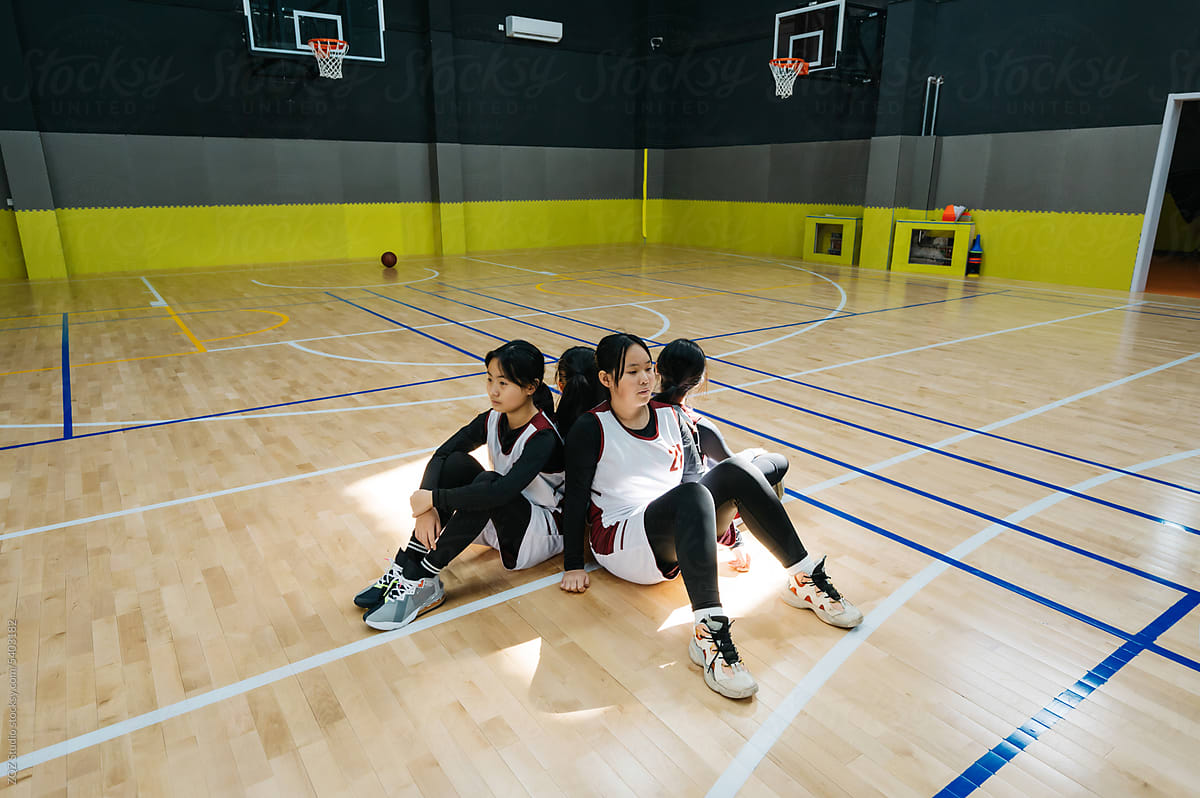 Teenager girls sitting back to back in school gym