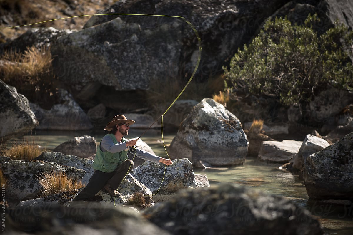 Man fly fishing in mid-cast with rocks and stream