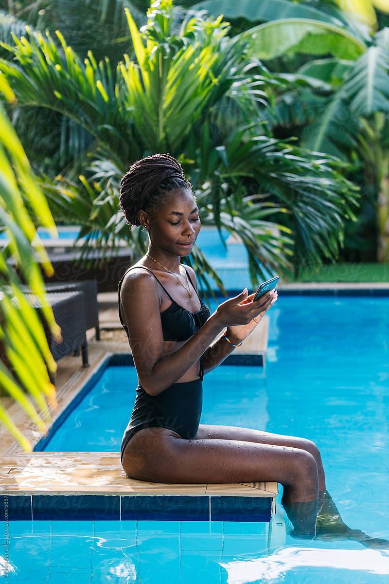African woman sitting on edge of swimming pool