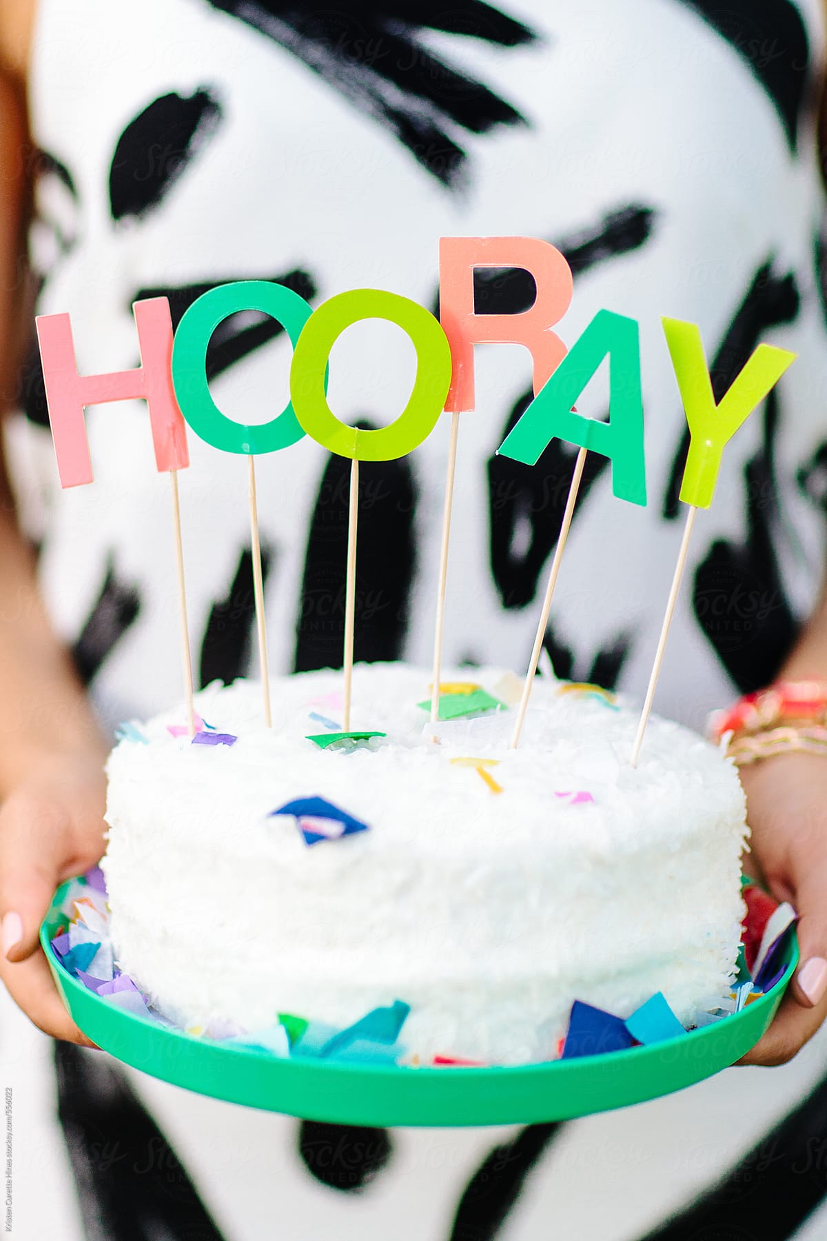 A woman holding a white cake that has the word HOORAY on the top