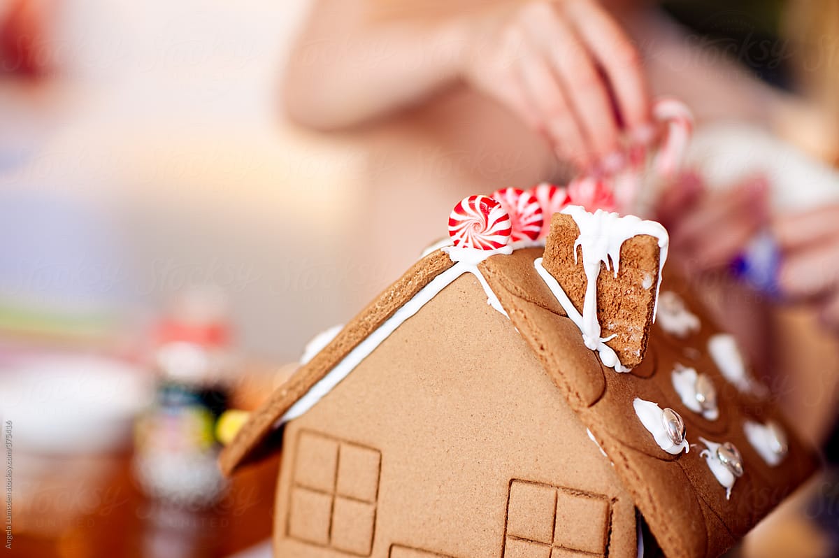 Close up of a gingerbread house being decorated by two young children