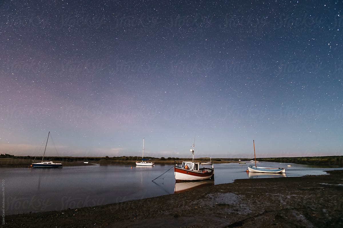 Boats under stars on a moonlit night. Burnham Overy Staithe, Norfolk, UK.