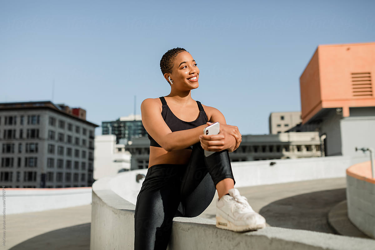 Fit Woman in Workout Clothing Sits on Building Rooftop and Listens to Music
