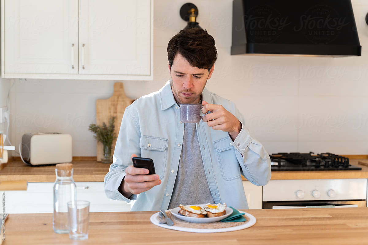 Portrait of happy man having breakfast and using phone