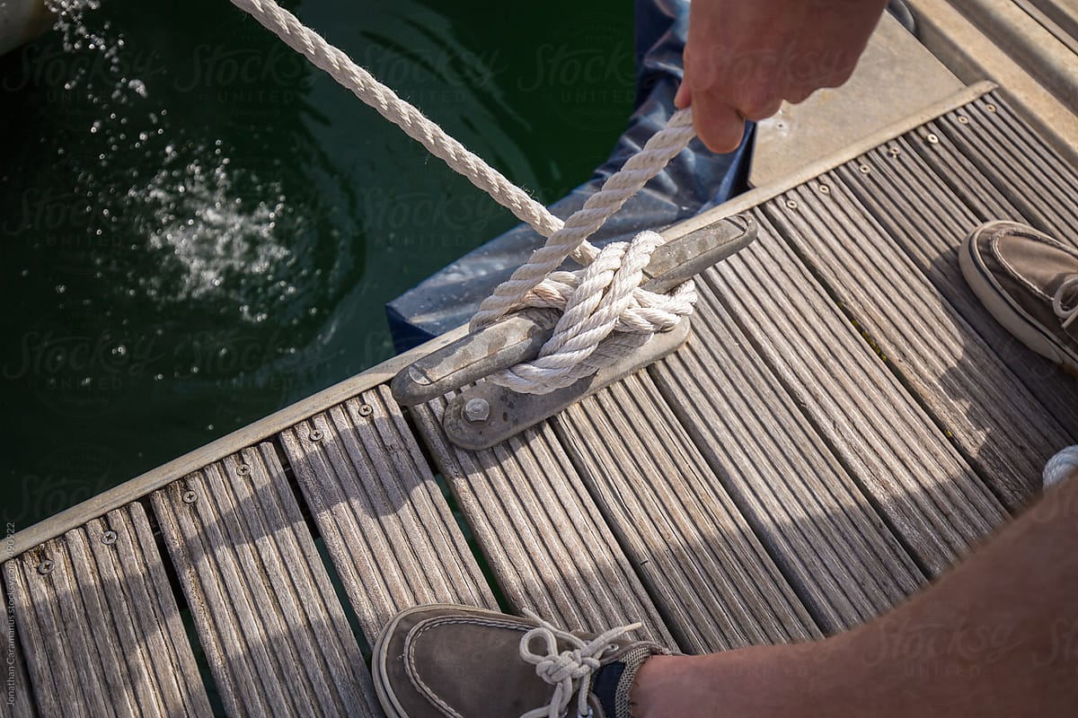 Hands tying a cleat hitch knot on wooden deck to moor boat in dock