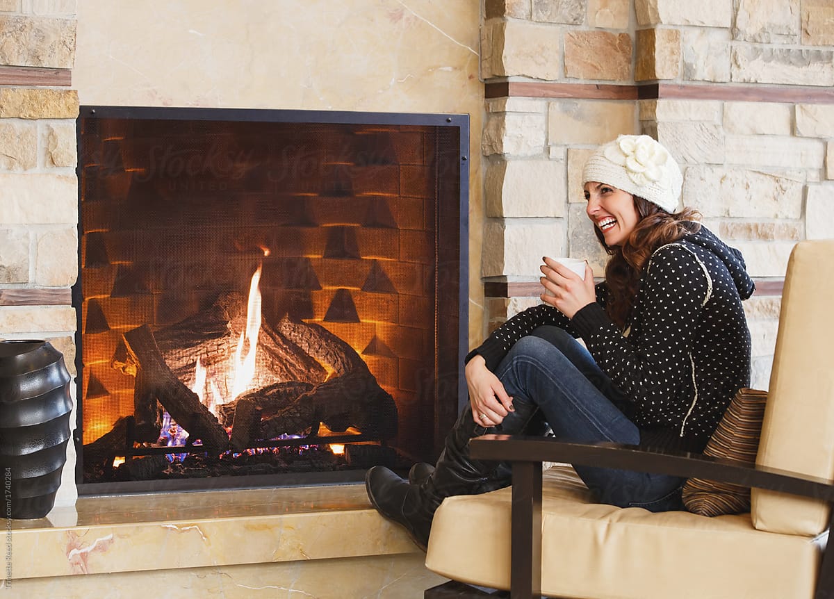 Woman sitting by fire drinking hot chocolate at ski lodge resort