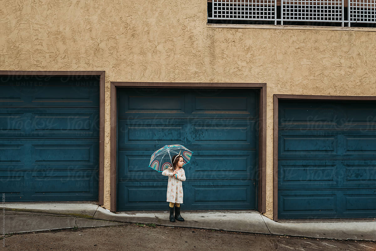 4 year old girl with rainbow umbrella standing on rainy day