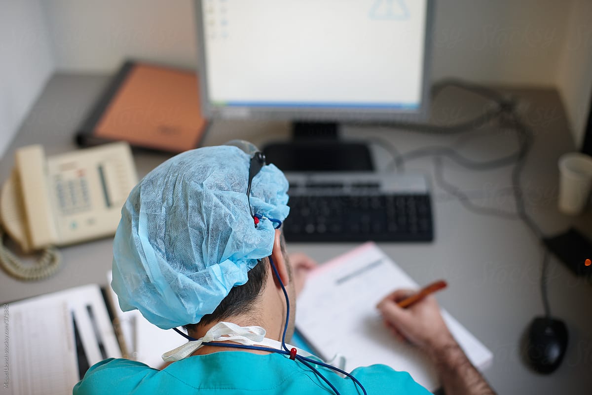 Anonymous doctor is handwriting at a patient medical history at desk.