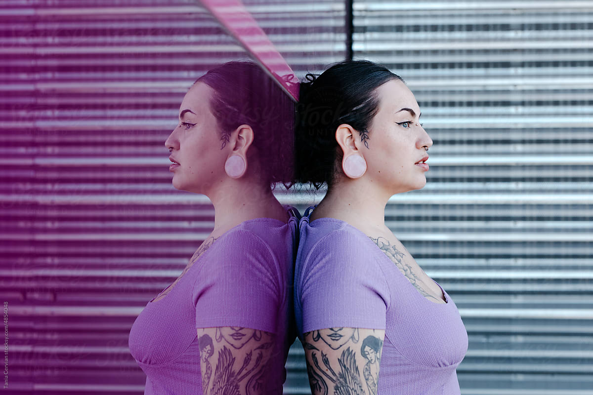 Tattooed curve model leaning on pink glass wall