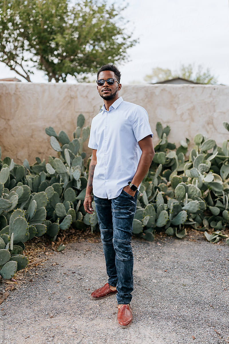 An African American male standing infront of a garden of cacti.