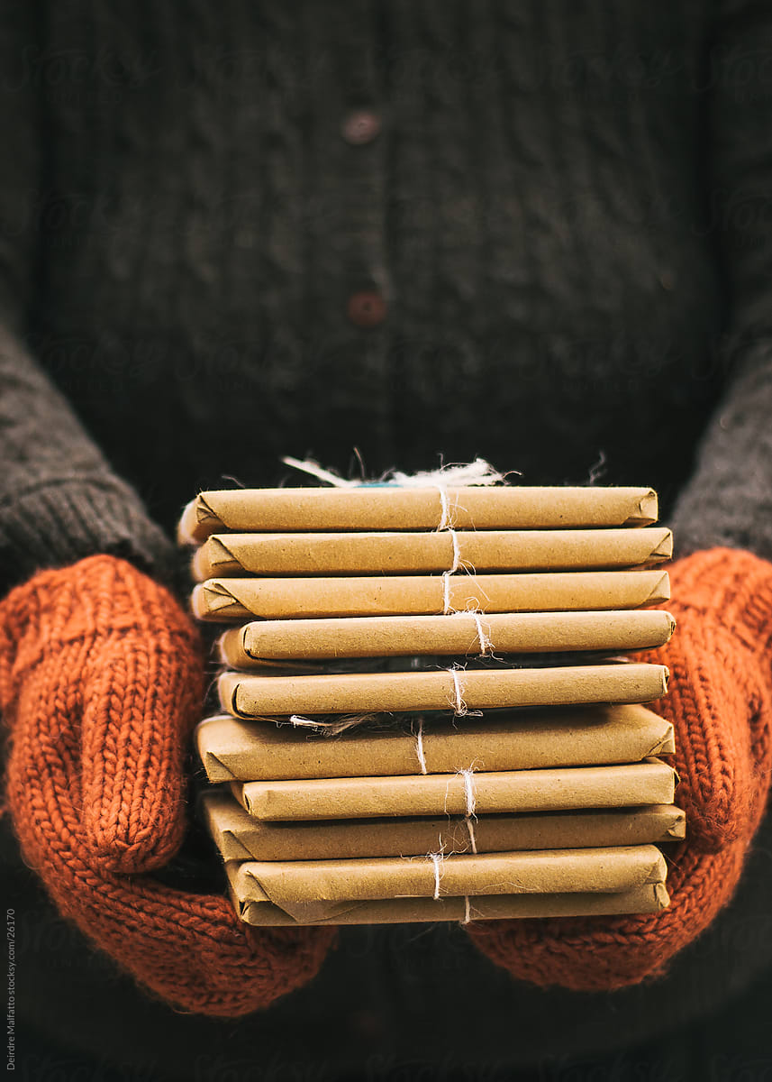 Mittened hands holding a stack of brown paper packages