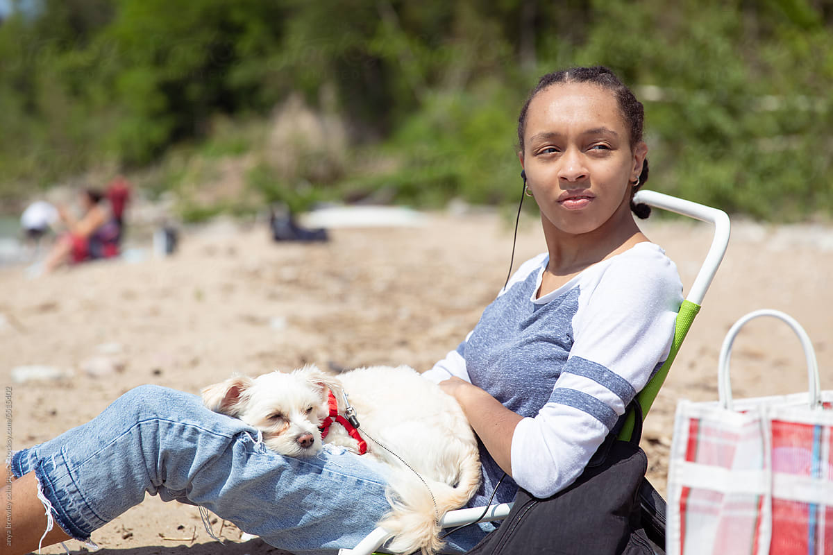 Teenager sitting on a beach chair with her pet dog lying on her lap
