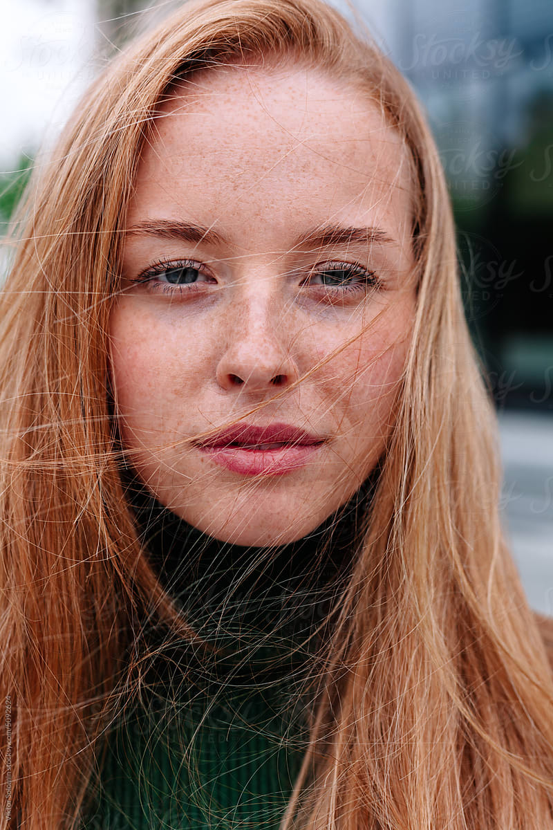 Young ginger woman with freckles looking at camera. Windy weather
