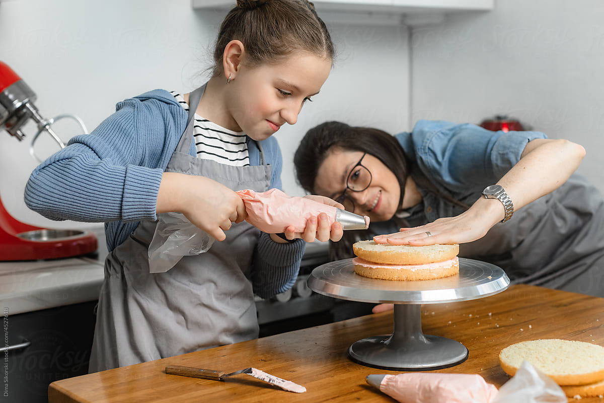 The daughter prepares a pink cake under the supervision of her mother