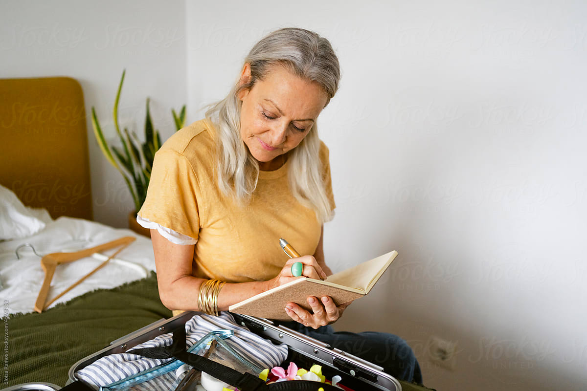 Gray-haired woman checking list by travel luggage