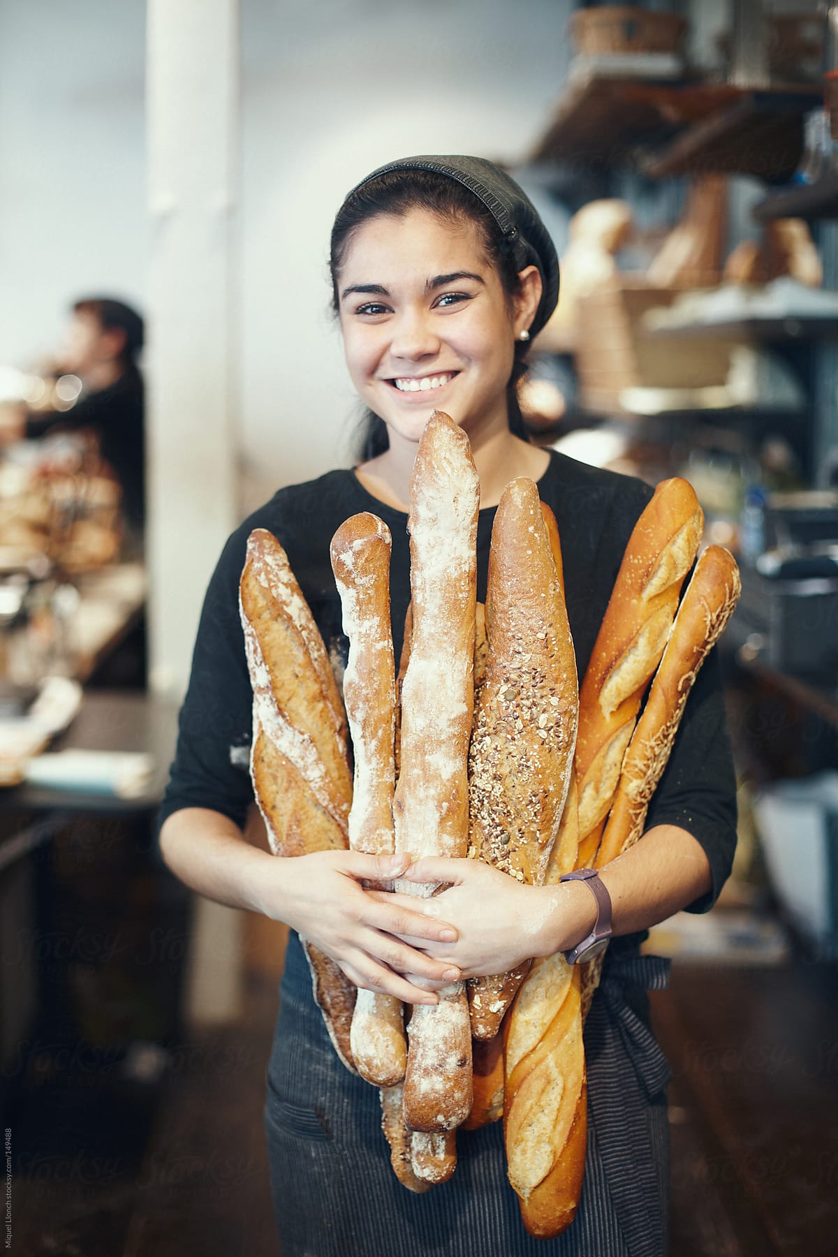 Young smiling saleswoman holding a variety of fresh French baguettes