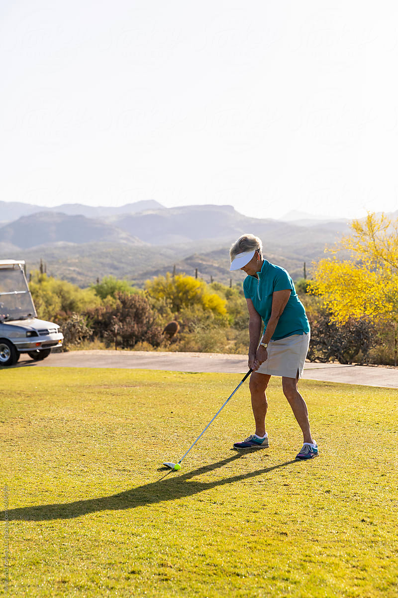 Senior Citizen Woman lines up golf shot on fairway