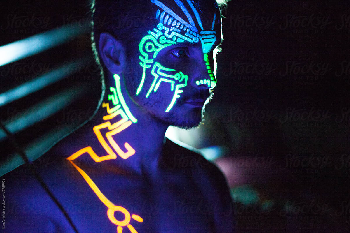 Young man painted in fluorescent paint on face and muscular torso