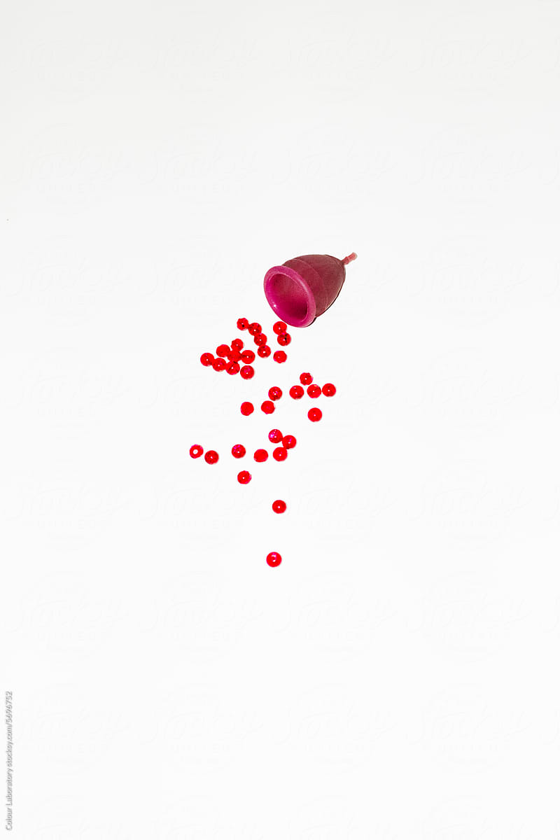 Conceptual period photo of period cup and red pearls as blood