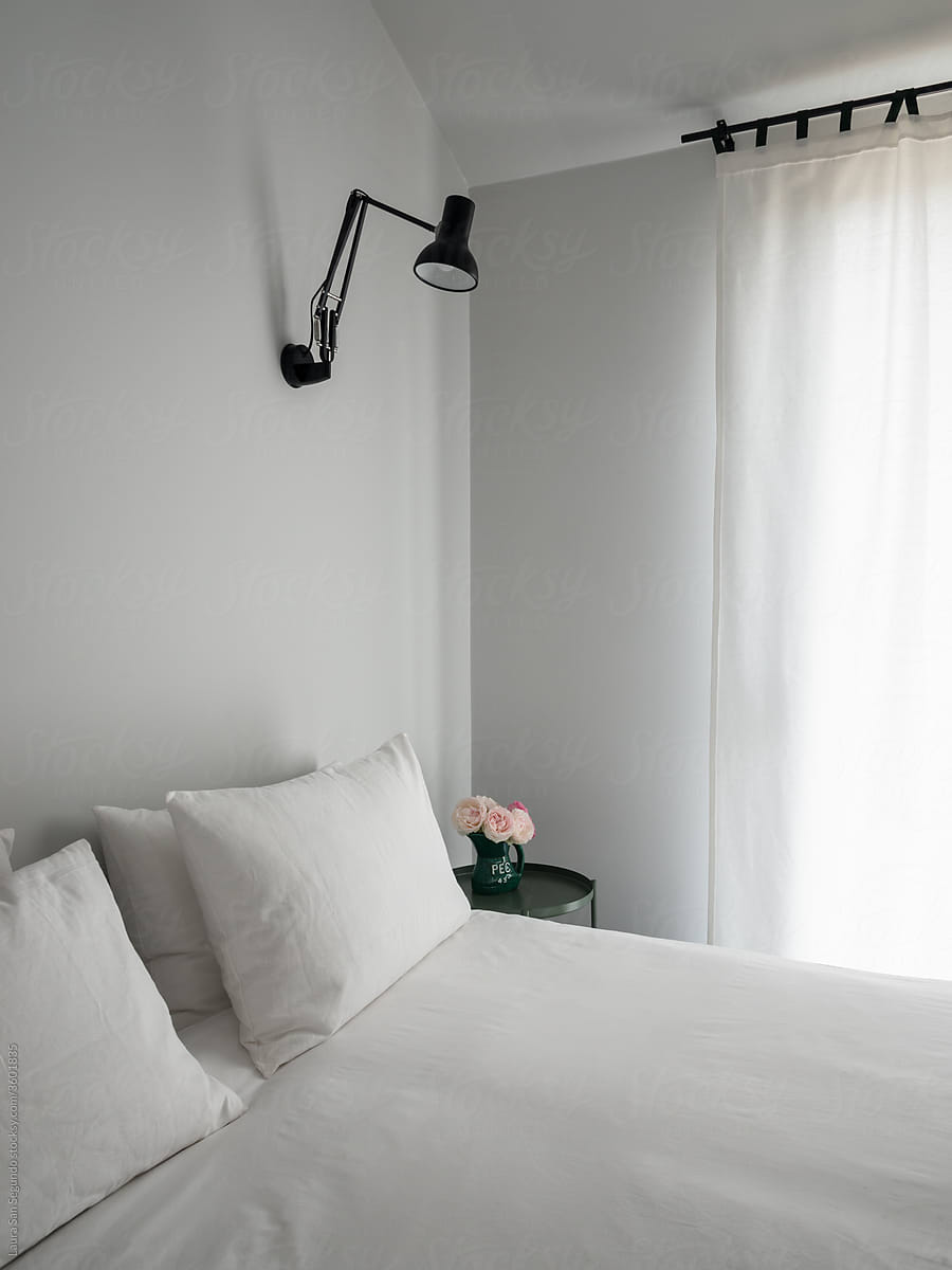 Minimalistic bedroom with a bed and a bedside table with flowers next to a window