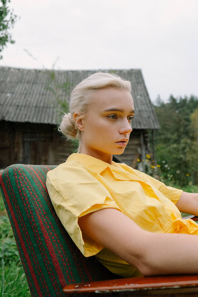 portrait of a pensive girl in a yellow retro dress who sits in a chair in nature