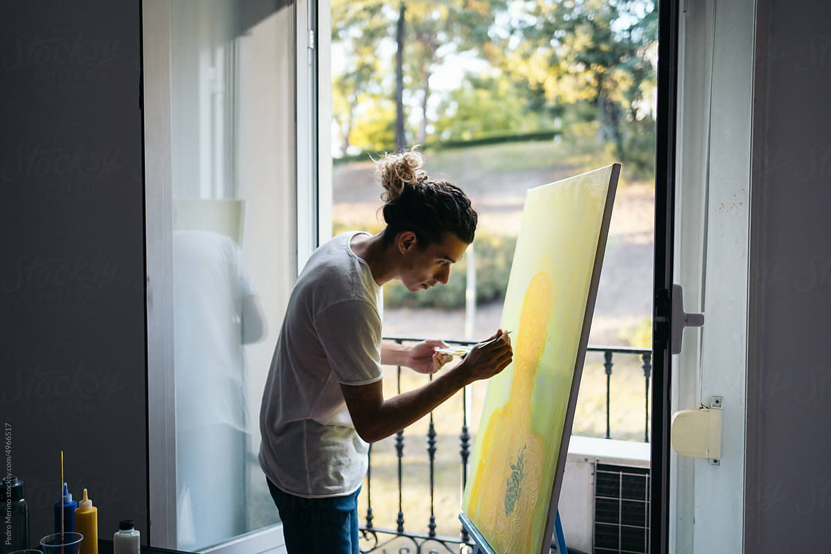 Young artist painting a canvas near a balcony