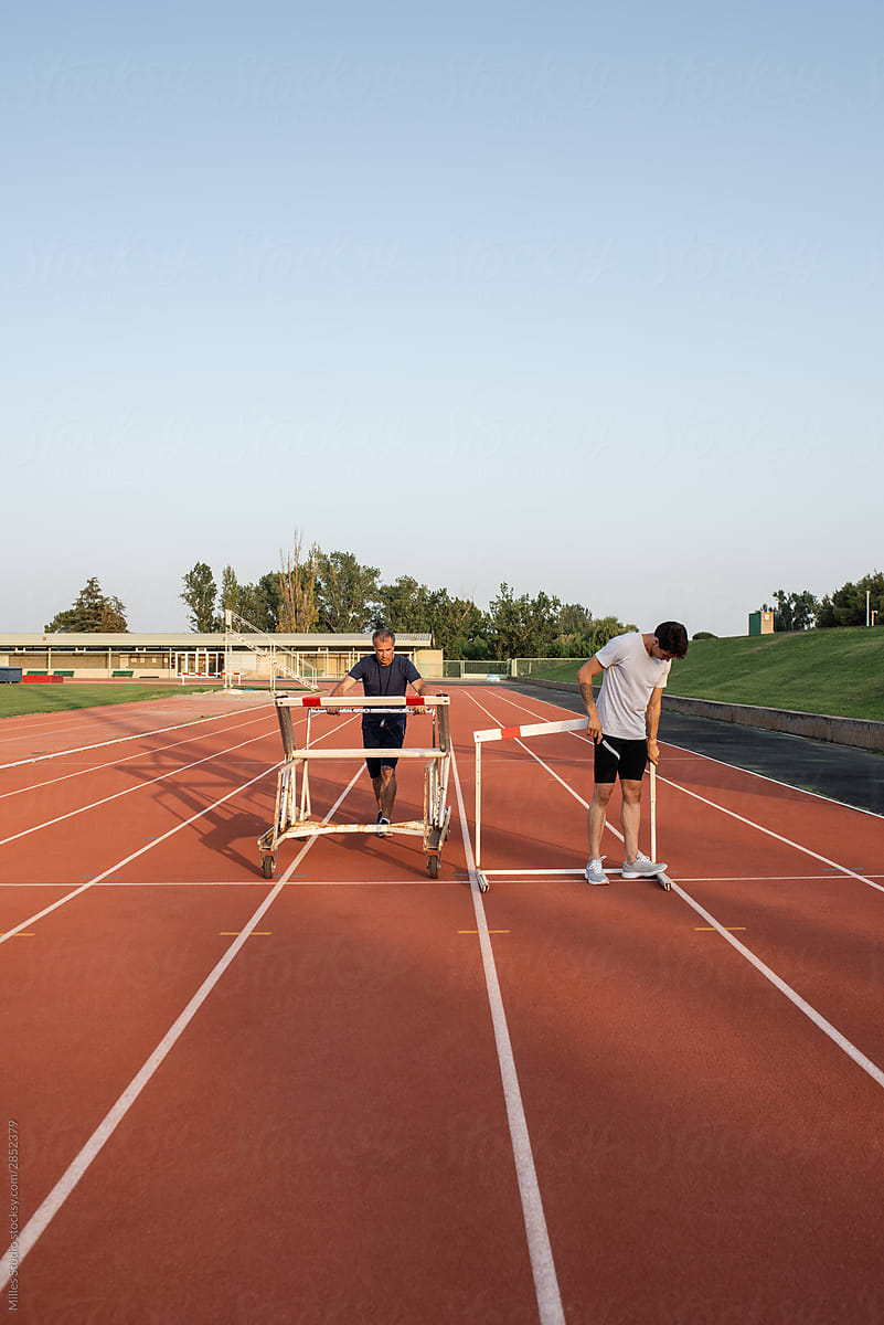 Trainer and athlete arranging hurdles on track