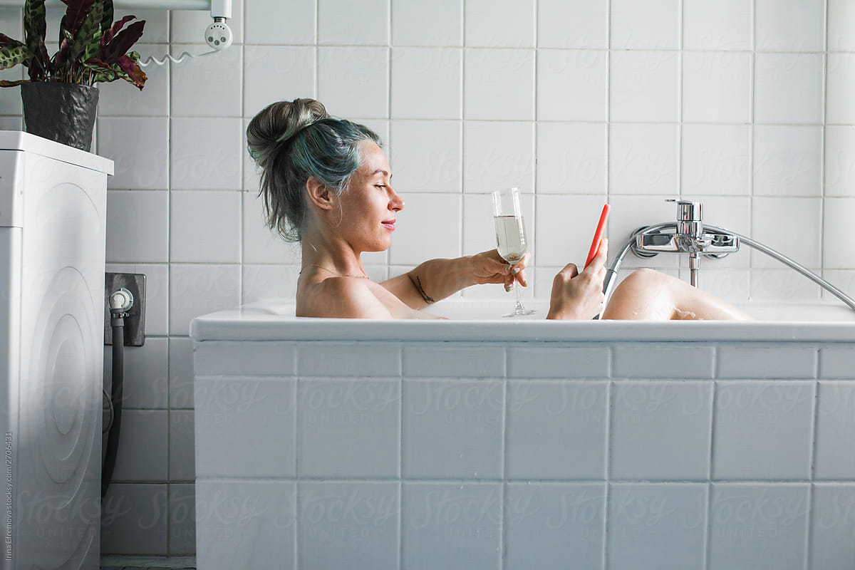 Blue Haired Woman With A Drink And Her Smartphone In A Bathtub By
