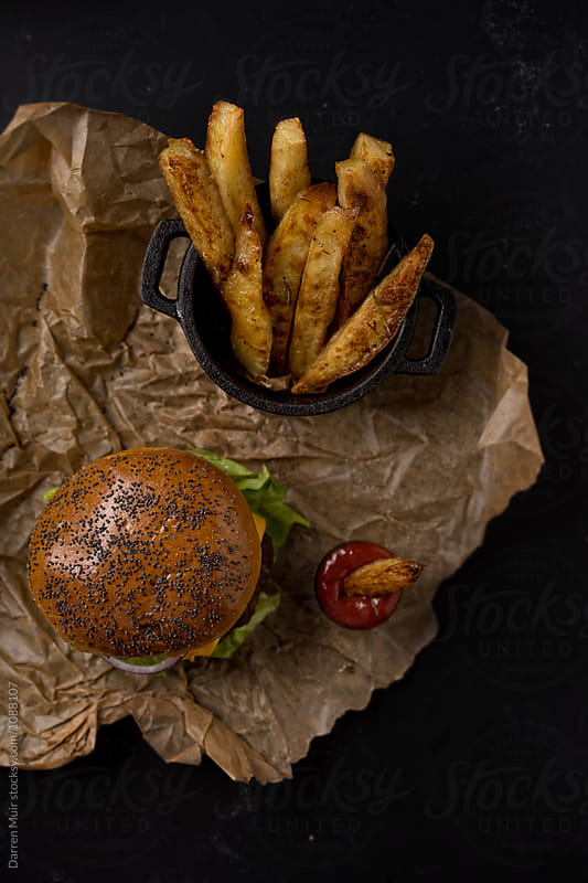 Burger and fries on brown paper on a dark background.