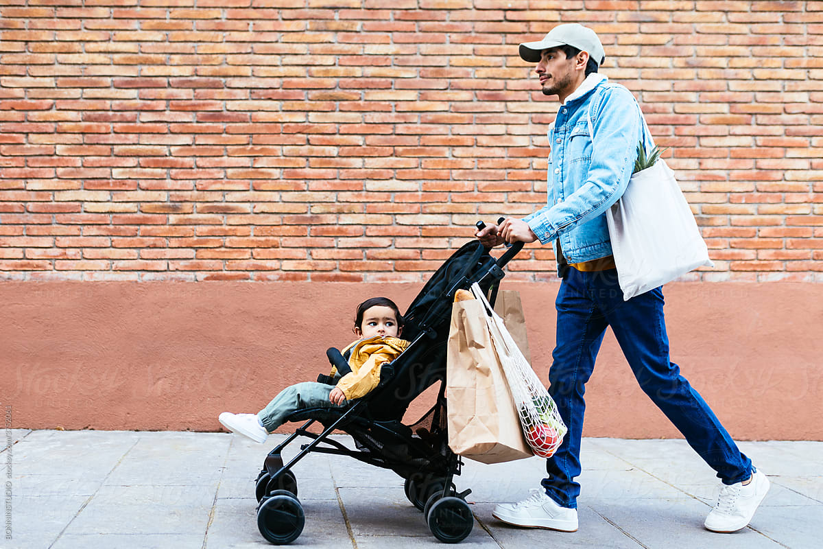 Indian father with baby walking near brick wall after shopping