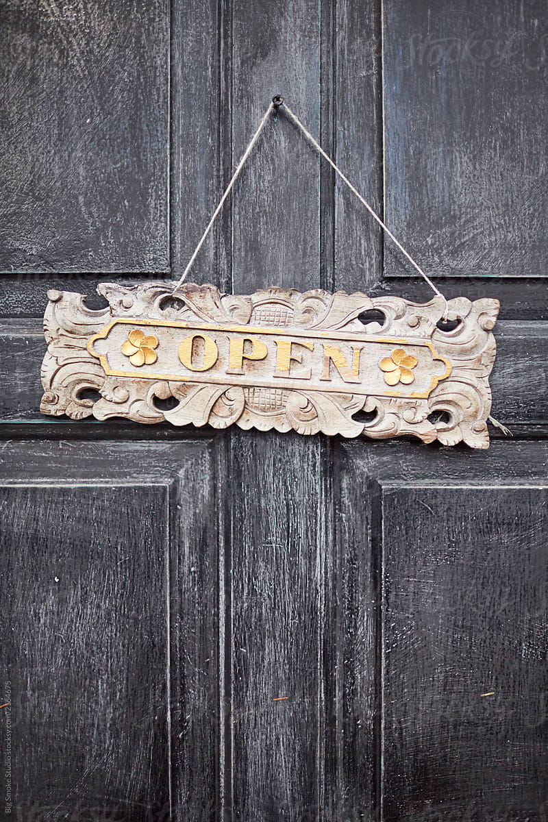 Close Up of Old Wooden Textured Door with Open Sign Against White Wall.