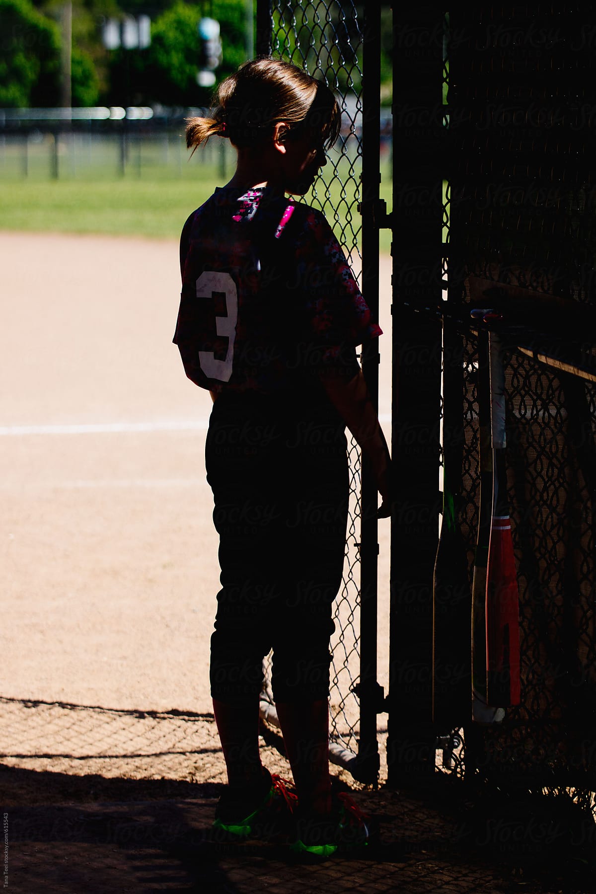 Young softball player stands in shadows of dugout
