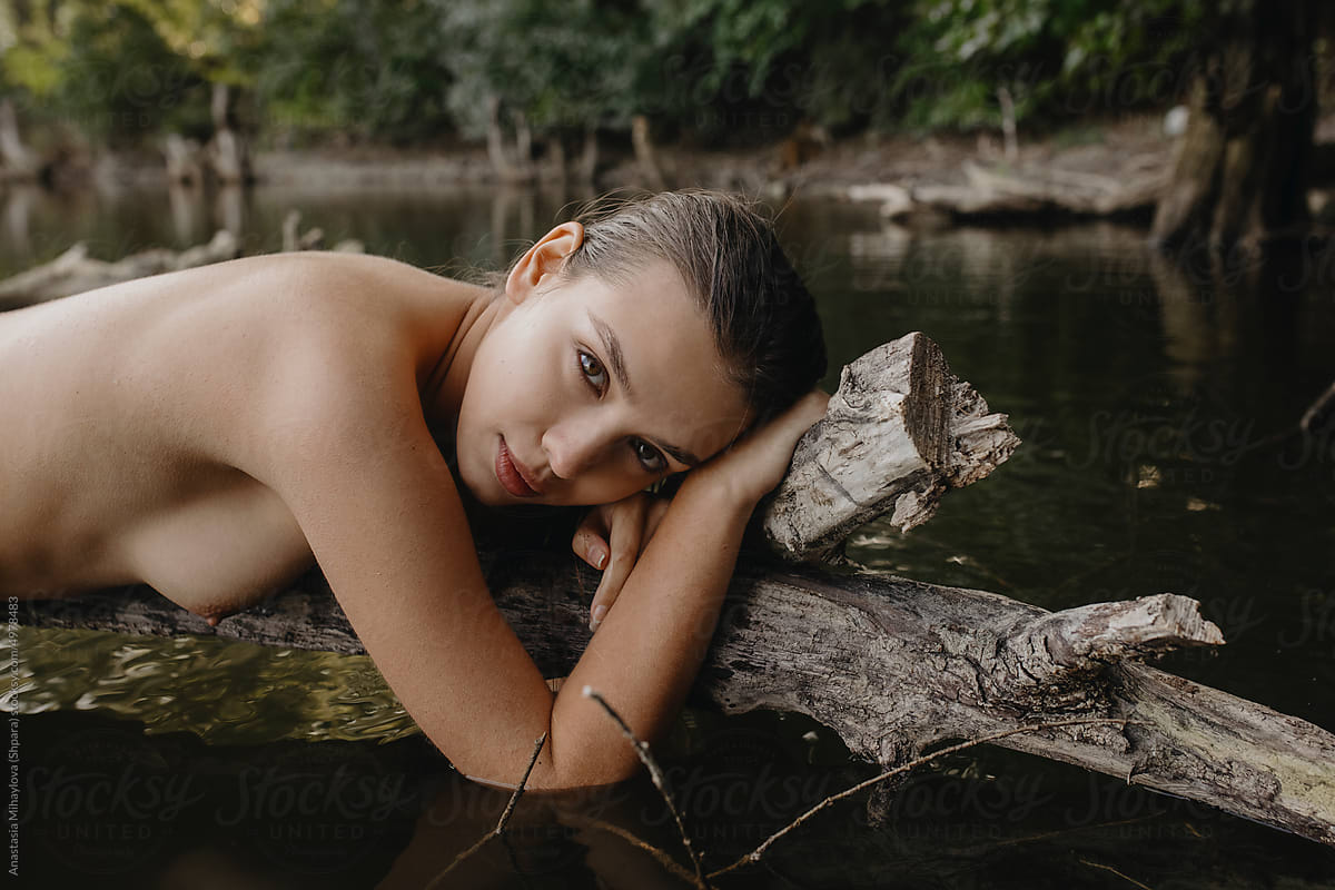 Portrait of naked woman lying on the tree in pond lake water