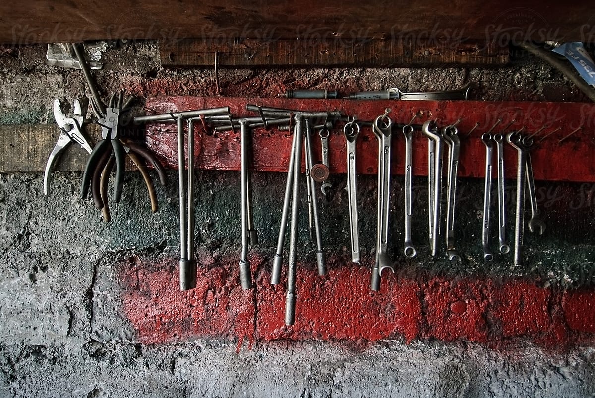 Old and partially broken tools hanging on the wall with red paint.