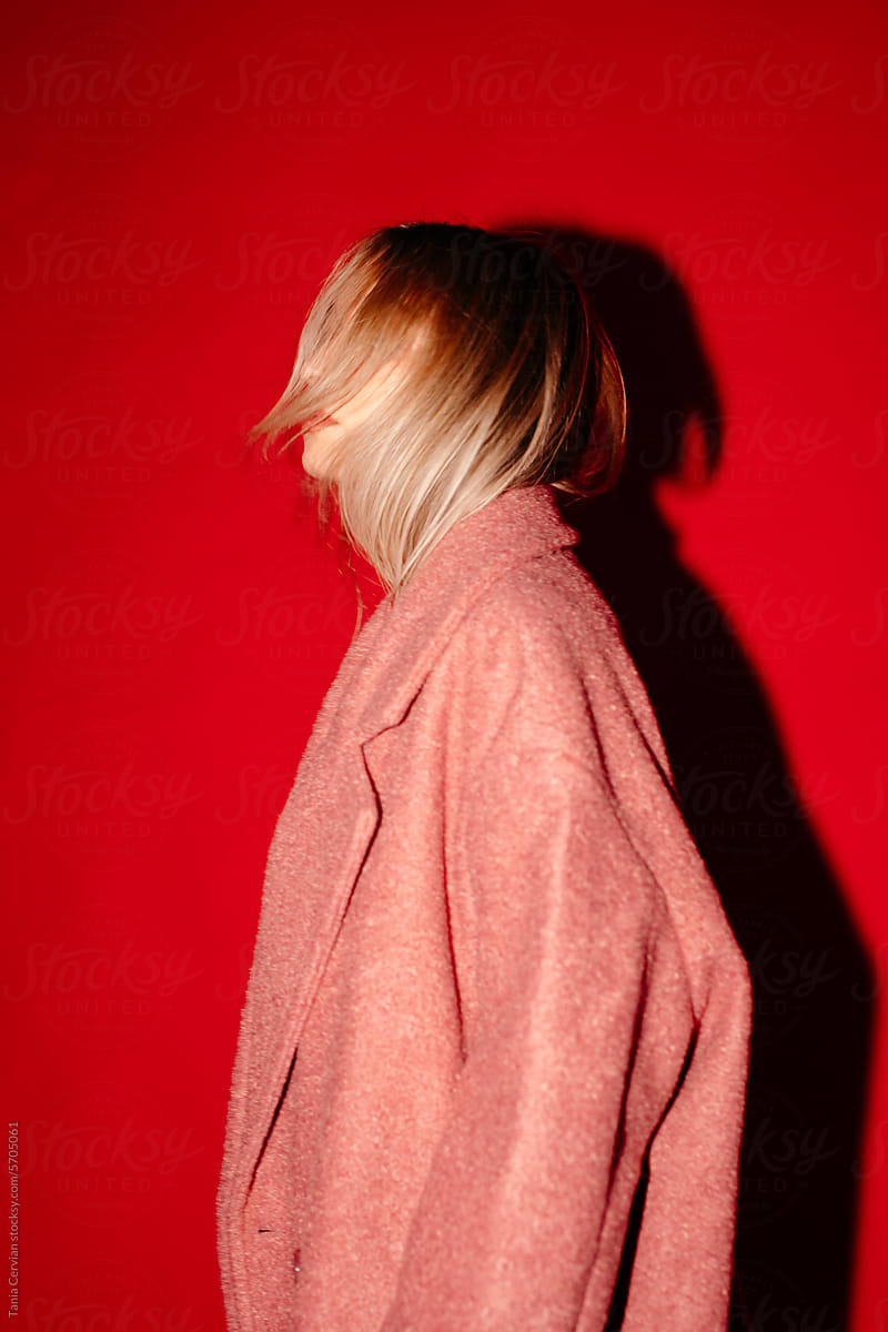 Anonymous woman in pink coat standing against red wall