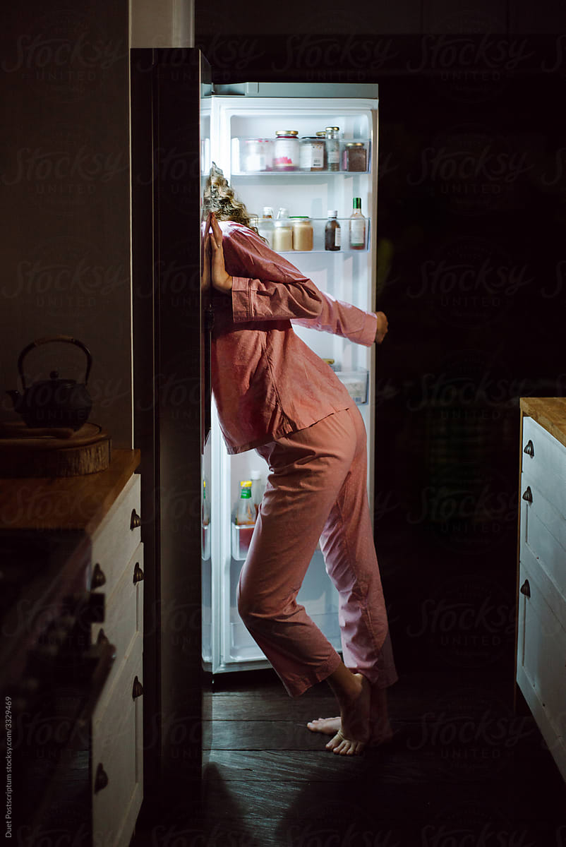 Girl in pajamas looks into the refrigerator in the kitchen at night