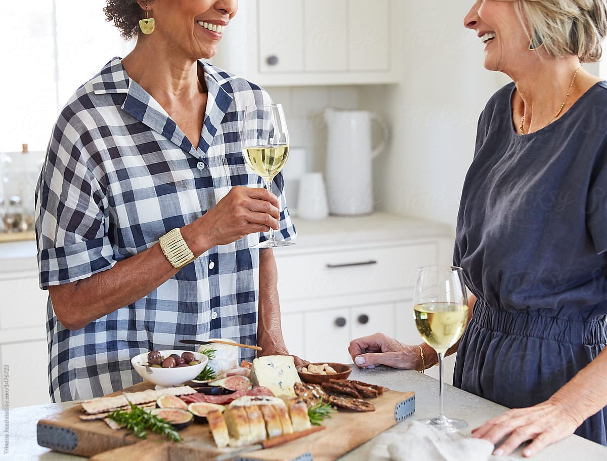Senior women friends drinking wine in kitchen