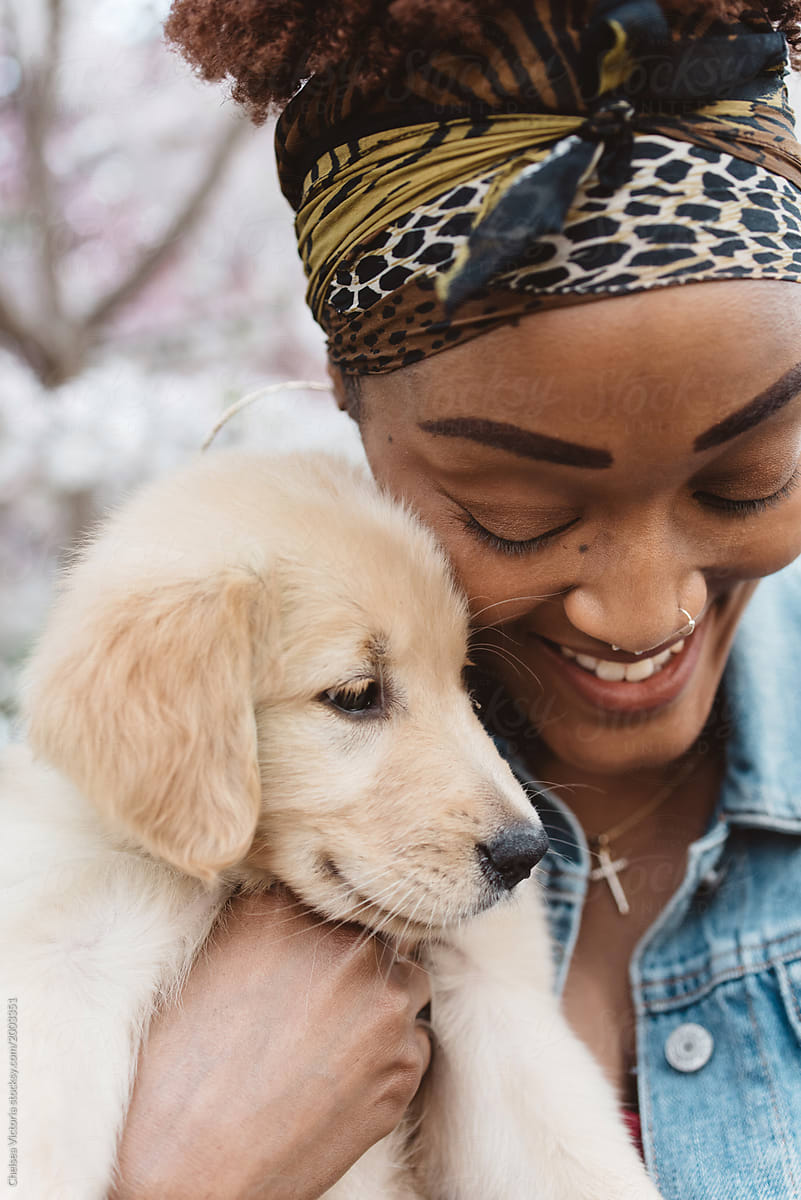 A black woman in her twenties holding her golden retriever puppy dog