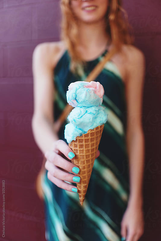A young woman eating a waffle cone with cotton candy in it